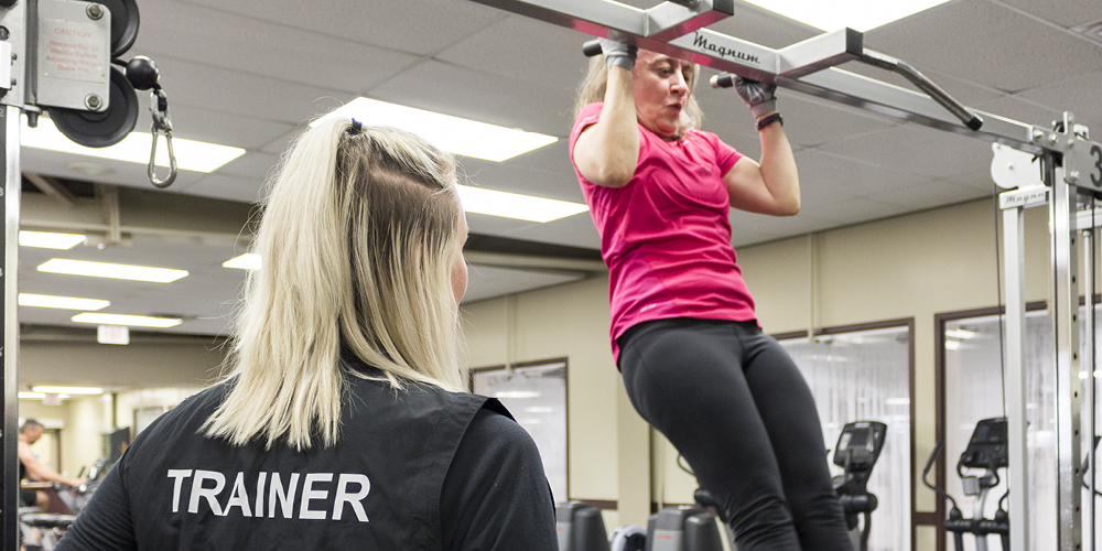 Woman doing pullups supervised by a trainer