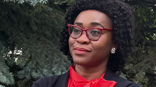 Sheika poses outside wearing a bold, fashionable red shirt and matching glasses